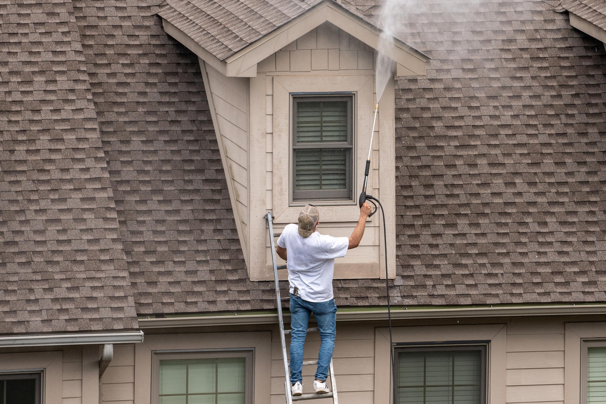 painter on a ladder using pressure washer spray to clean woodwork before painting townhome